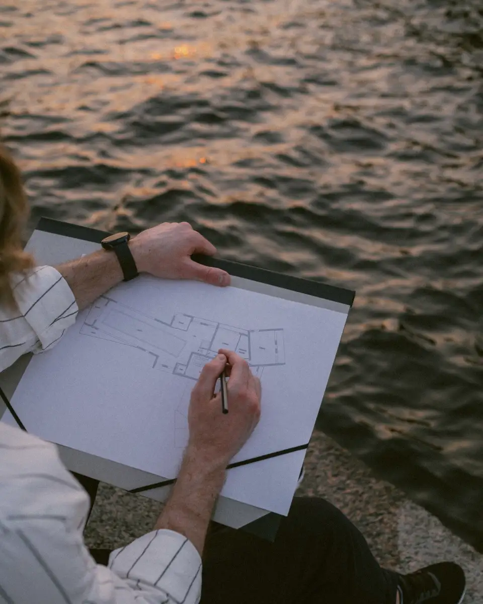 A designer sketching a plan outdoors by the water