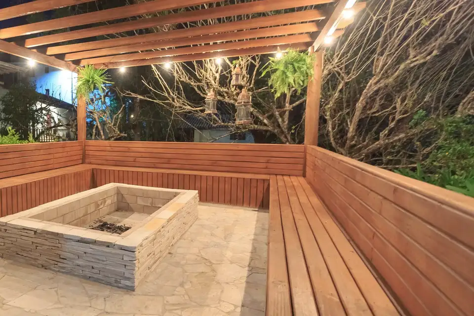 A covered wooden terrace with built-in benches around a stone fire box