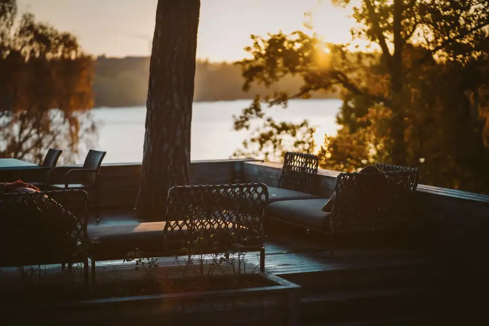 A terrace with woven chairs overlooking a lake at sunset
